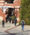 Students with backpacks, seen from behind, walking toward a red brick campus building with white pergola details on a sunny day.