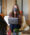 A woman in a mask sitting down in a chair with her laptop talking to another woman.