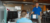 An employee in a blue Click Rain polo chats with and stands next to a man sitting at his desk working.