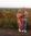 Ella, with her husband and dog, smile at the camera in front of fall foliage.