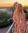 Audrey standing on a deck while wearing a colorful dress. There are buildings and palm trees behind her.