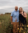 Renae and her partner posing in a field with tall grass and wildflowers. Her partner's arm is around her shoulders.